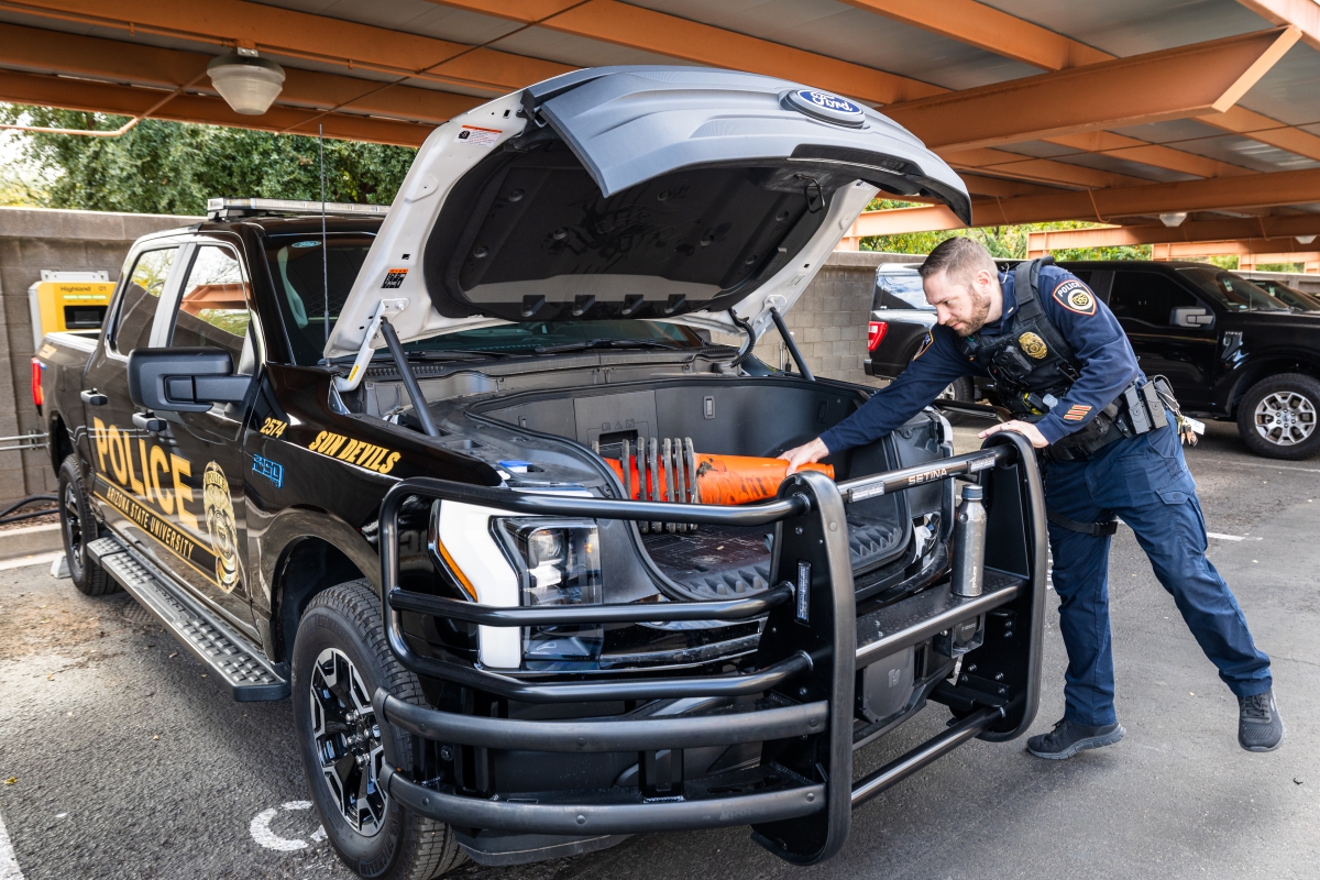 Police officer moving orange traffic cones in a front trunk of a truck.